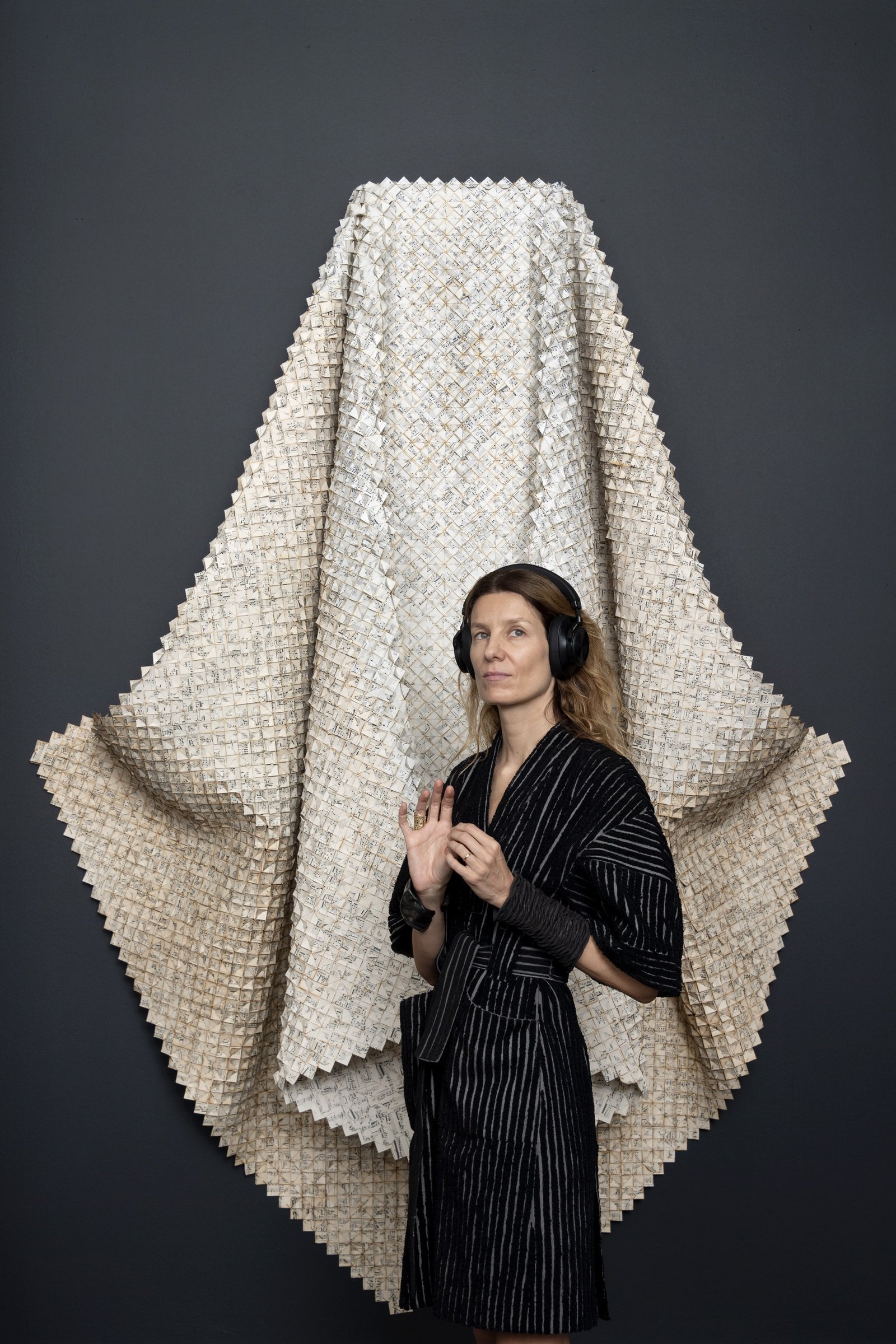 Catalina Swinburn stands in front of Das Lied von der Erde (The Song of the Earth) by Gustav Mahler, 2018/2019, a woven paper piece made of music score pages using Chinese poetry by Li Bai, Meng Haoran, Qian Qi &amp; Wang Wei of the Tang Dynasty. 230h x 180w x 55d cmCourtesy of Catalina Swinburn Studio and Selma Feriani Gallery